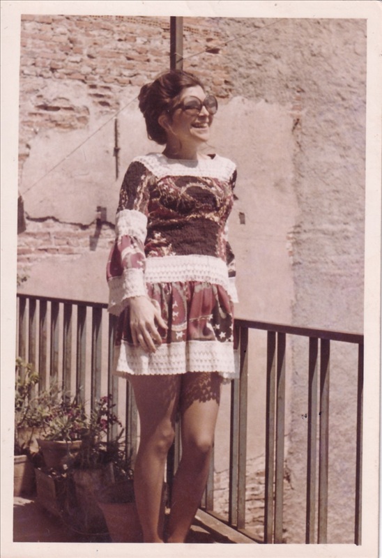 1970'ler modası desenli ve dantel detaylı mini elbise giyen, büyük güneş gözlüklü kadın tuğla duvarlı balkonda gülümserken