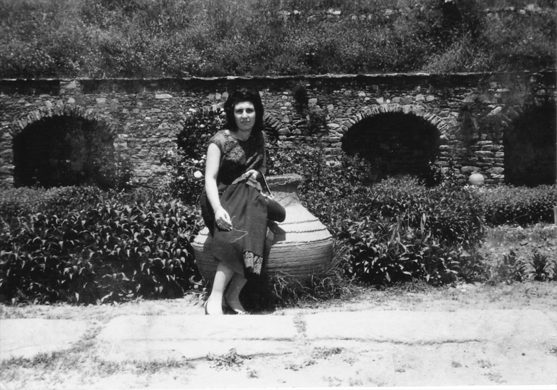 Tarihi taş duvarlı bahçede büyük toprak küp üzerine oturmuş şık elbiseli nostaljik kadın fotoğrafı