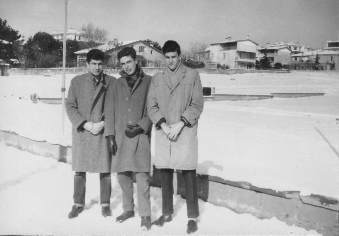 Karlı bir günde kalın kışlık paltolarıyla yan yana durarak poz veren üç genç erkek